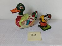 Photo of vintage tin duck and golfing panda wind-up toys showing their colorful painted metal surfaces and standing on a white textured surface.