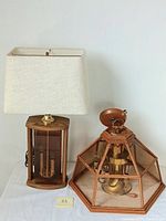 Photo of the two lamps side-by-side: wooden framed table lamp with fabric shade and hanging wooden framed glass ceiling lamp.