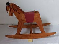Side view of wooden rocking horse with red saddle and fabric mane and tail.