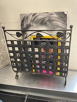 Front view of bronze finished metal magazine rack containing magazines, showing leaf embellishments and lattice sides.