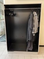 Front view showing black interior with hanging rod, black wooden hangers, and some garments hanging inside for scale only.
