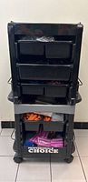 Front view of black plastic rolling salon accessory tower with multiple drawers and 'Professional Choice' branding, showing stored hair rollers inside drawers.