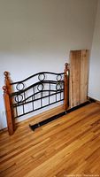 Bed frame disassembled, showing metal headboard with circular decorative elements and wooden posts leaning against wall with wood slats.