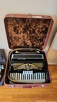 Opened accordion in brown vinyl hard case showing overall instrument and strap