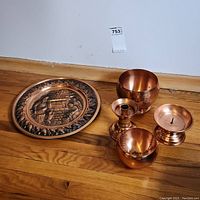 Group photo of the decorative copper plate, candle holder, hanging bowl, and smaller bowl displayed on wooden floor.