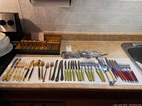 Wide view of various cutlery sets arranged on kitchen counter showing multiple types of handles and materials.