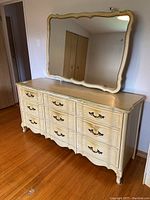 Full view of 9 drawer dresser with attached decorative mirror showing the cream finish and bronze handles.