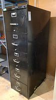 Full view of a tall black metal filing cabinet with 5 drawers, with visible scratches and scuffs.