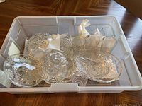 Crystal glassware including glasses, cream and sugar set, and serving dishes inside a plastic bin.