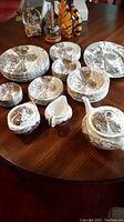 Full set arranged showing plates, bowls, teapot, cream, sugar, coasters, and saucers with Staffordshire scenic pattern.