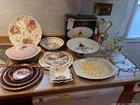 Various plates, trays, and bowls arranged on a kitchen counter showing floral and decorative patterns.