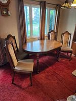 Wide shot showing oval wooden dining table with four upholstered wooden chairs around it in a living room.