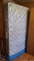 Front view of mattress wrapped in plastic, showing white top with patterned design