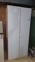 Front view of white laminate two-door wardrobe cupboard, showing closed doors with white handles.
