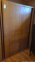 Full view of the laminate wardrobe cabinet with two sliding doors and metal handles, showing woodgrain finish.
