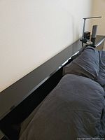 Side view of the black headboard with a couch in front, showing smooth flat surface and glossy finish