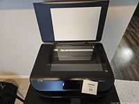 Front and top angled view of open scanner lid showing flatbed scanner surface of black HP Envy 5055 printer.