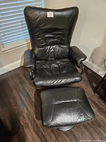 Full front view of black leather reclining chair with matching ottoman under it.