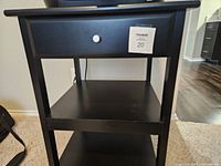 Front view of the black printer table showing the drawer and shelves with a MaxSold tag attached.