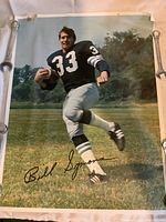 Poster showing Bill Symons in Toronto Argonauts uniform number 33 holding a football in action pose with signature and visible wear on edges