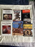 Photo of six anatomy, physiology, nutrition, and exercise physiology related reference books laid out on a light surface.
