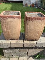 Pair of square ceramic torches outside on patio wall, showing textured beige and brown finish