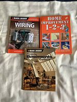 Photo showing three home improvement books laid flat on a white surface: Blacks & Decker Wiring guide, Home Improvement 1-2-3, and Blacks & Decker Finishing Basements Edition.