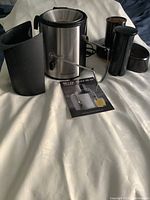 Big Boss stainless steel and black plastic electric juicer with separate parts arranged including instruction manual and cleaning brush.
