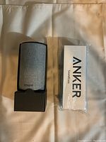 Amazon Echo smart speaker partially lifted from base, Anker Soundcore speaker box wrapped in plastic.