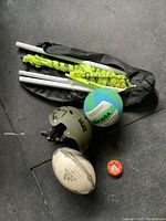 Photo showing rugby ball, volleyball, helmet, football, floor hockey puck, and badminton net case with poles.