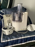 Moulinex food processor with clear lid, handle, feed tube, and instruction manual set on cushion.