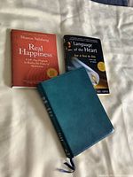 Photo showing the front covers of the three books: a teal leather-bound Bible, "Real Happiness" by Sharon Salzberg, and "Language of the Heart" by Joel Cooper.