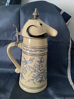 Side angle view of 12 inch West End Brewing Company ceramic stein with character head lid and blue floral decorations on body