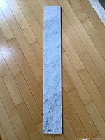 Full view of the elongated rectangular white marble slab laid on wooden floor showing natural veining and polished surface.