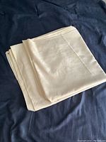 Folded cream polyester tablecloth laid on dark blue fabric showing texture and neat folds.