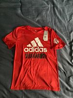 Front view of red Adidas youth shirt with large white logo and Toronto FC crest on sleeve, showing condition and tags.