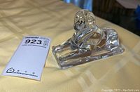 Side view of clear crystal Baccarat sphinx figurine on a table with yellow cloth.