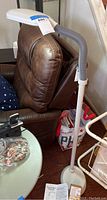 Full view of the white Bell & Howell sunlight floor lamp standing beside a brown chair showing height and structure.