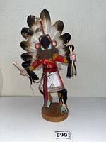Front and side views of the Chasing Star Kachina doll showing costume colors, feather headdress, and item held in hands with visible artist signature.