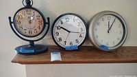 Three clocks on wooden shelf: vintage Arbor Emory mantle clock and two modern wall clocks