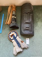 Three wood-carved African masks and fiber wall art displayed on carpet