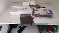 Apple Mini iPad in colorful protective case, user manual, charging cable and power adapter arranged on shelf.
