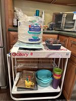 Front view of the Polder metal kitchen cart with kitchen items including paper plates, mixing bowls, plastic cups, muffin pan cooling racks and others.