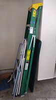 Side view of green six-foot extension ladder with two metal step ladders and folded card table leaning against a wall