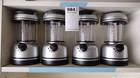 Photo showing four silver and black battery-powered lanterns lined up on a shelf, highlighting their identical design and condition.