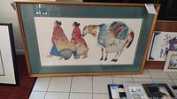 Full view of large framed western print with horse and two people in colorful attire, framed with green matte and gold wood.