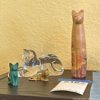 Four animal figurines displayed on wooden tray against yellow wall: Lenox crystal lion, MMA brass lion, marble cat, soapstone cat