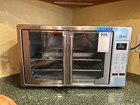 Front view of Oster toaster oven TSSTTVFDDG-C-035 closed, showing dual glass doors and handles.