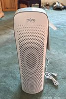 Front view of white Purezone air purifier standing upright on carpet, showing perforated air intake grille and electrical cord.