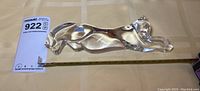 Full view of the entire crystal cat figurine lying on fabric background, showing its length and sleek form, with ruler included for scale.